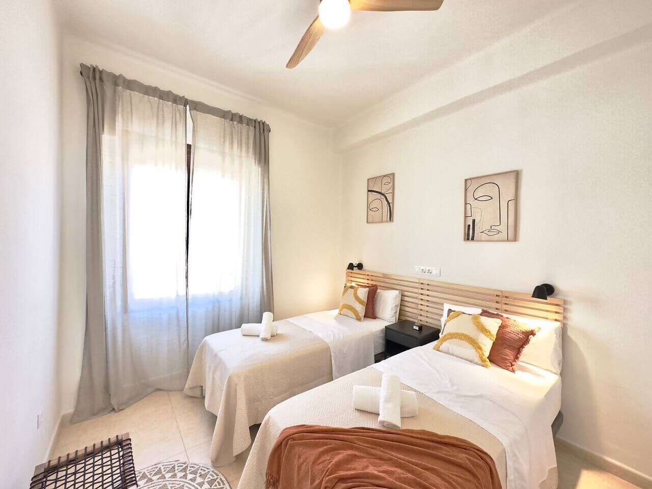 Een hotelkamer met twee bedden, een plafondventilator en kunstwerken aan de muur.