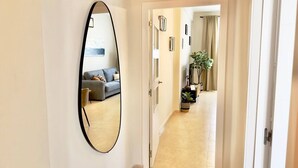 Un pasillo con un espejo grande, una puerta que da a una sala de estar con un sofá y una planta.