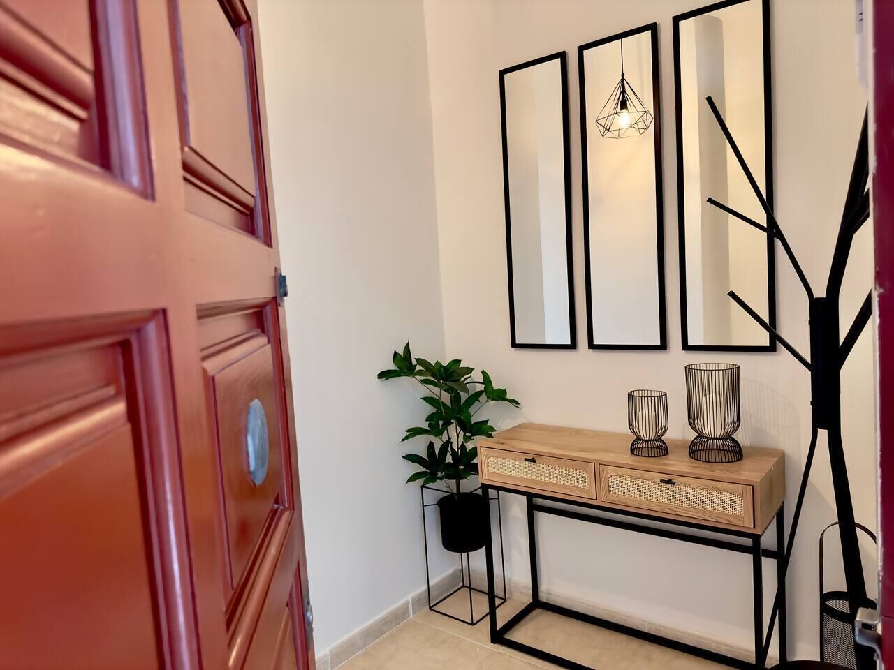 Un couloir avec une porte en bois, une console ornée d’objets décoratifs, une plante en pot, des miroirs fixés au mur et une suspension.