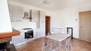 A modern kitchen with a gas stove, oven, and stainless steel cabinets. There is a dining table with clear chairs and a wooden door in the background. - Lovely apartment in Gubbio with WiFi (Gubbio)