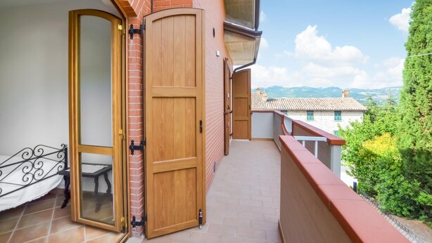 A balcony with a wooden door, a small table, and a view of a town and hills. - Lovely apartment in Gubbio with WiFi (Gubbio)