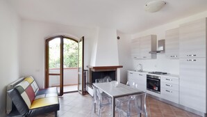 A modern kitchen with white cabinets, a gas stove, and a built-in oven. There is a dining table with clear chairs and a bench with colorful cushions. A fireplace is visible in the corner. - Lovely apartment in Gubbio with WiFi (Gubbio)