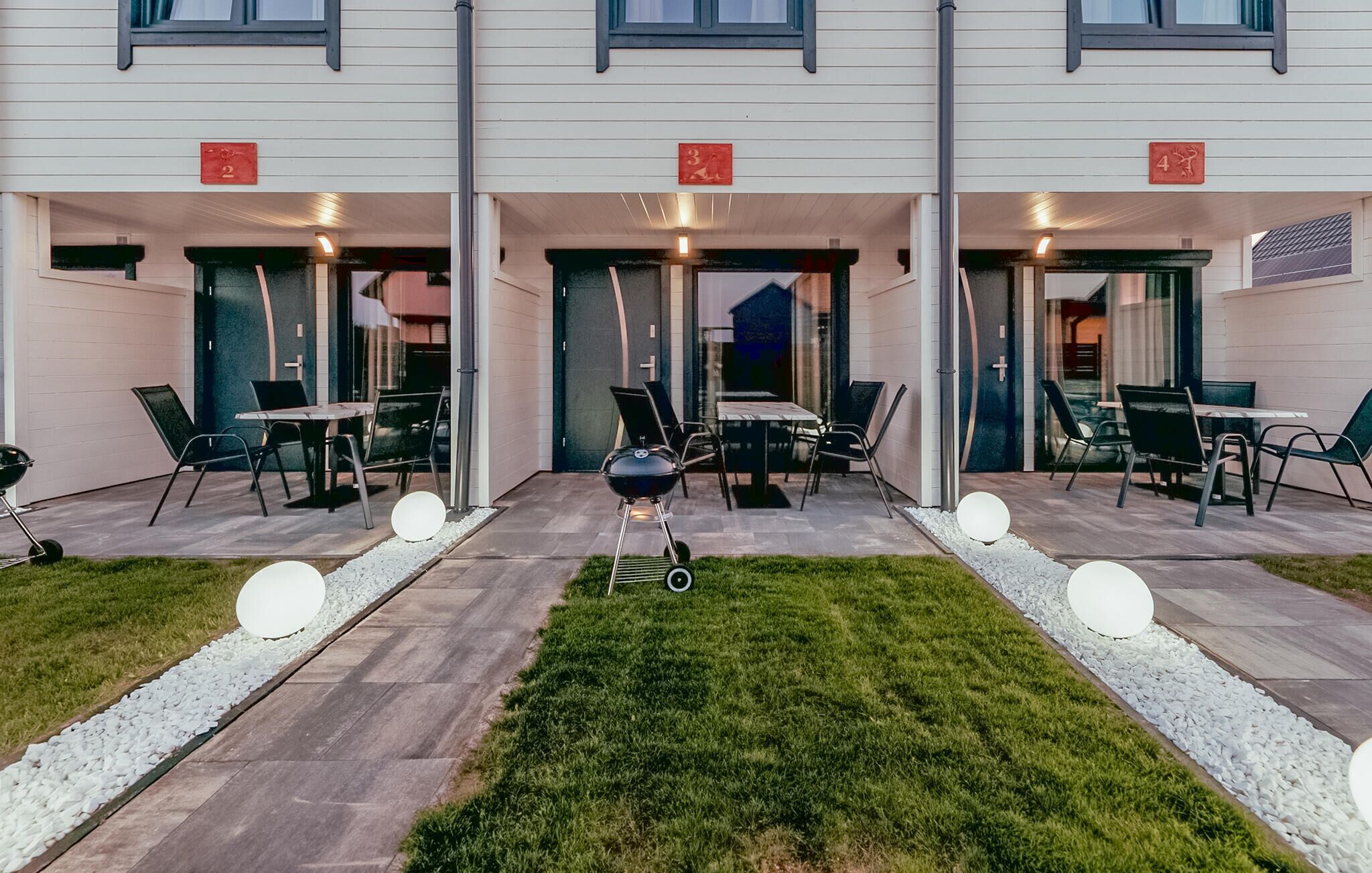 A building with numbered doors, outdoor seating, and a grill.