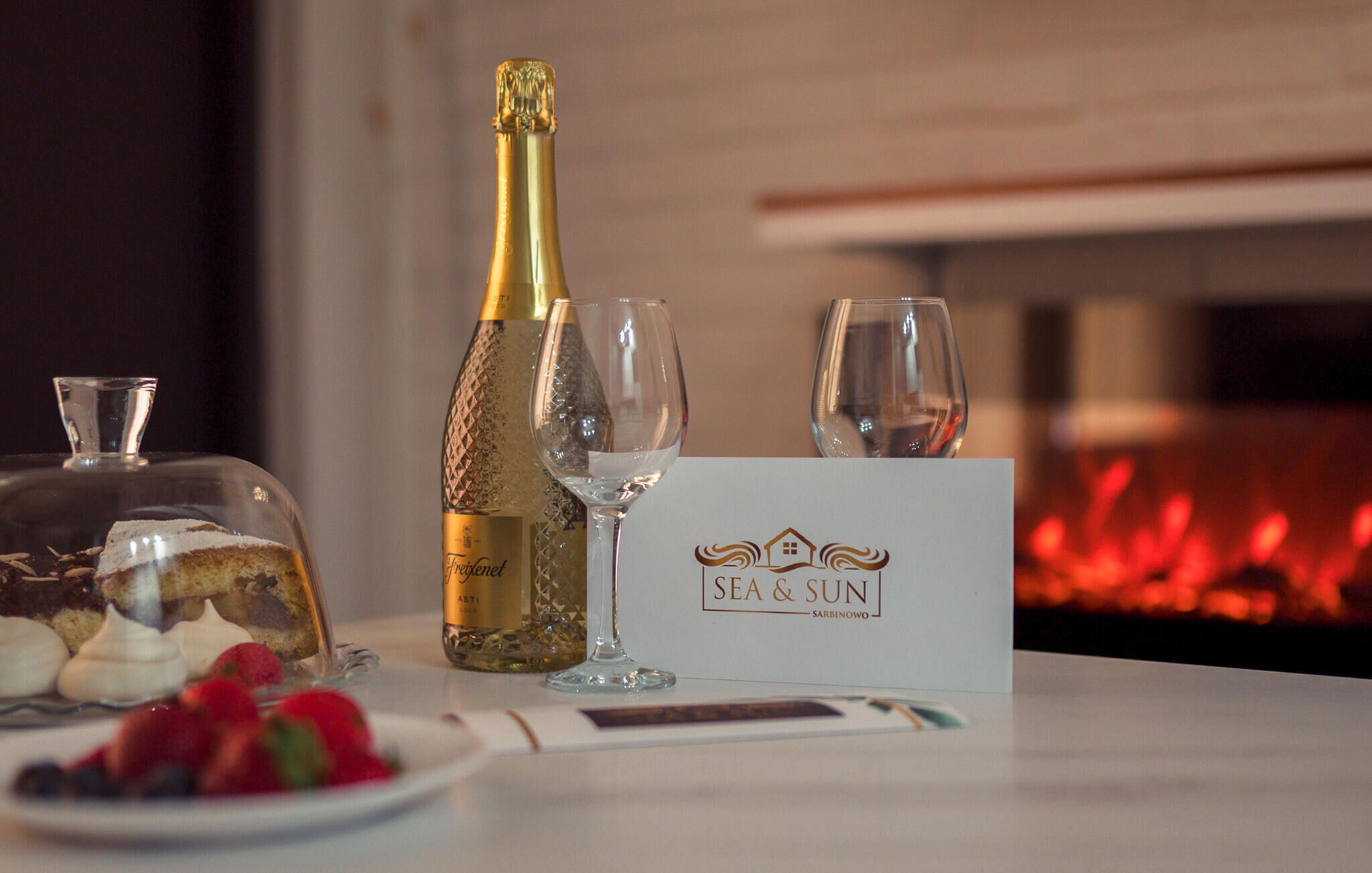A bottle of Freixenet Asti wine, two glasses, a dessert plate with strawberries, and a menu titled "SEA & SUN" in a restaurant setting.