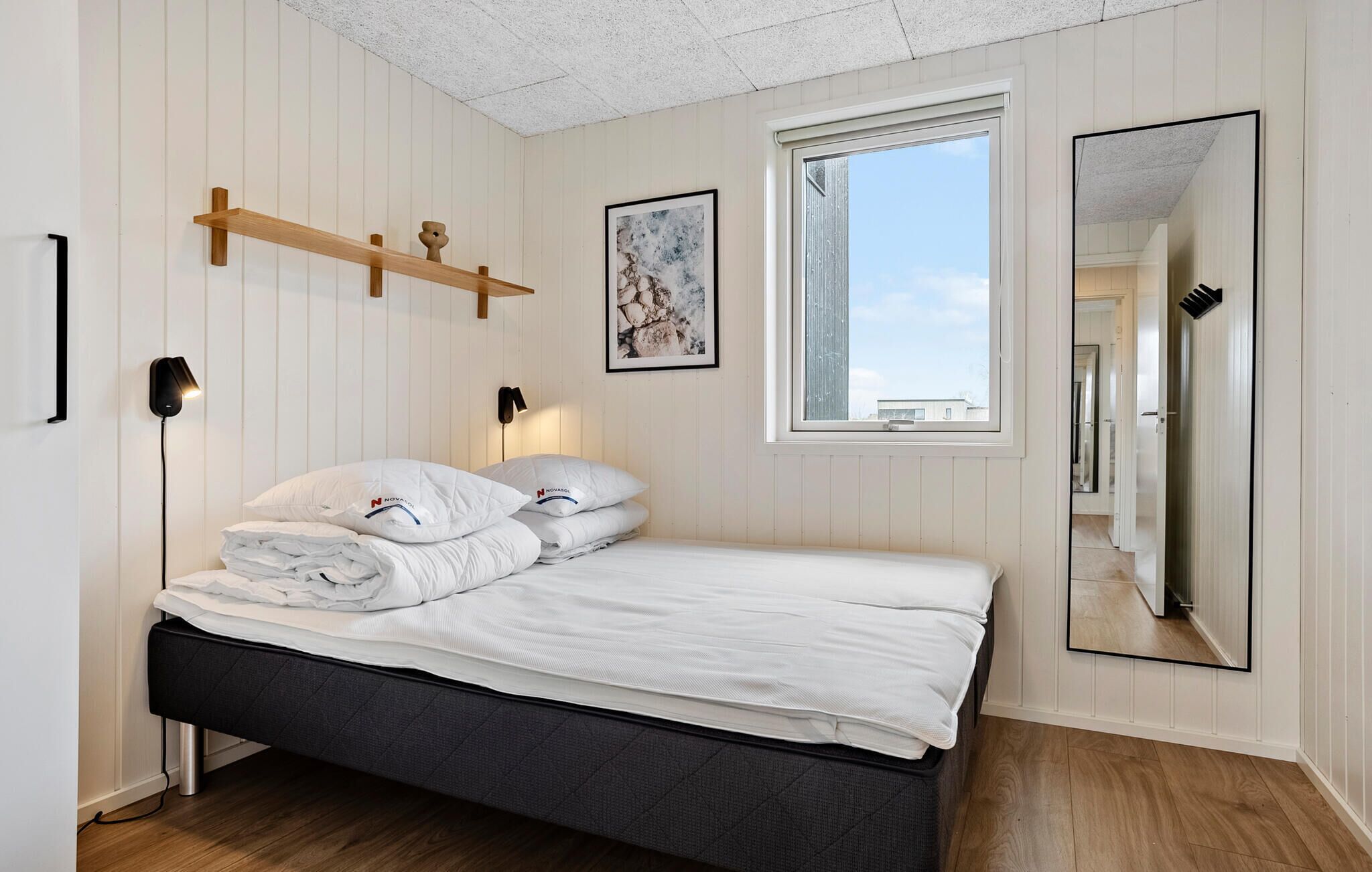 Quarto com cama, luminárias de cabeceira, janela e espelho.