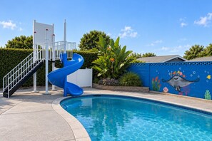 A swimming pool with a blue slide and a mural of a sea creature. - Pixar Pier: Heated Pool, Arcade, Golf, and More!+ (Garden Grove)