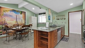 A kitchen with a large island, a dining area with a table and chairs, and a mural of the Eiffel Tower. - Pixar Pier: Heated Pool, Arcade, Golf, and More!+ (Garden Grove)