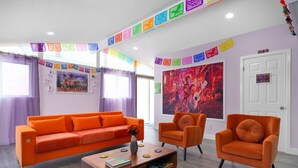 A modern living room with a bright orange sofa, two matching armchairs, and a wooden coffee table. - Pixar Pier: Heated Pool, Arcade, Golf, and More!+ (Garden Grove)