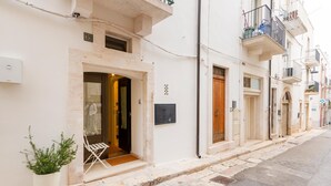 A row of white buildings with balconies, a potted plant, and a door with a window. - Tea Tree Apartments 1 (Castellana Grotte)