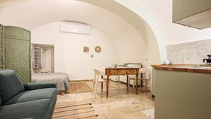 A compact living space with a kitchenette, a dining area, and a seating area with a sofa and chairs. - Tea Tree Apartments 1 (Castellana Grotte)