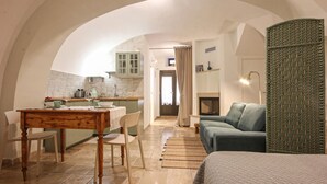 A cozy living room with a sofa, a dining table with chairs, and a kitchen in the background. - Tea Tree Apartments 1 (Castellana Grotte)