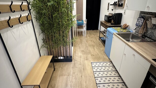 A modern kitchen with wooden flooring, a built-in bench, a large potted plant, and a small dining area. - Scilló House (Palermo)