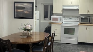 A kitchen with white cabinets, a dining table with chairs, a refrigerator, a microwave, and an oven.