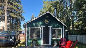 A small green house with a chimney, a porch with red chairs, and a GMC truck parked nearby.