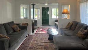 A living room with two grey sofas, a patterned rug, a lamp, and a green door leading to another room.