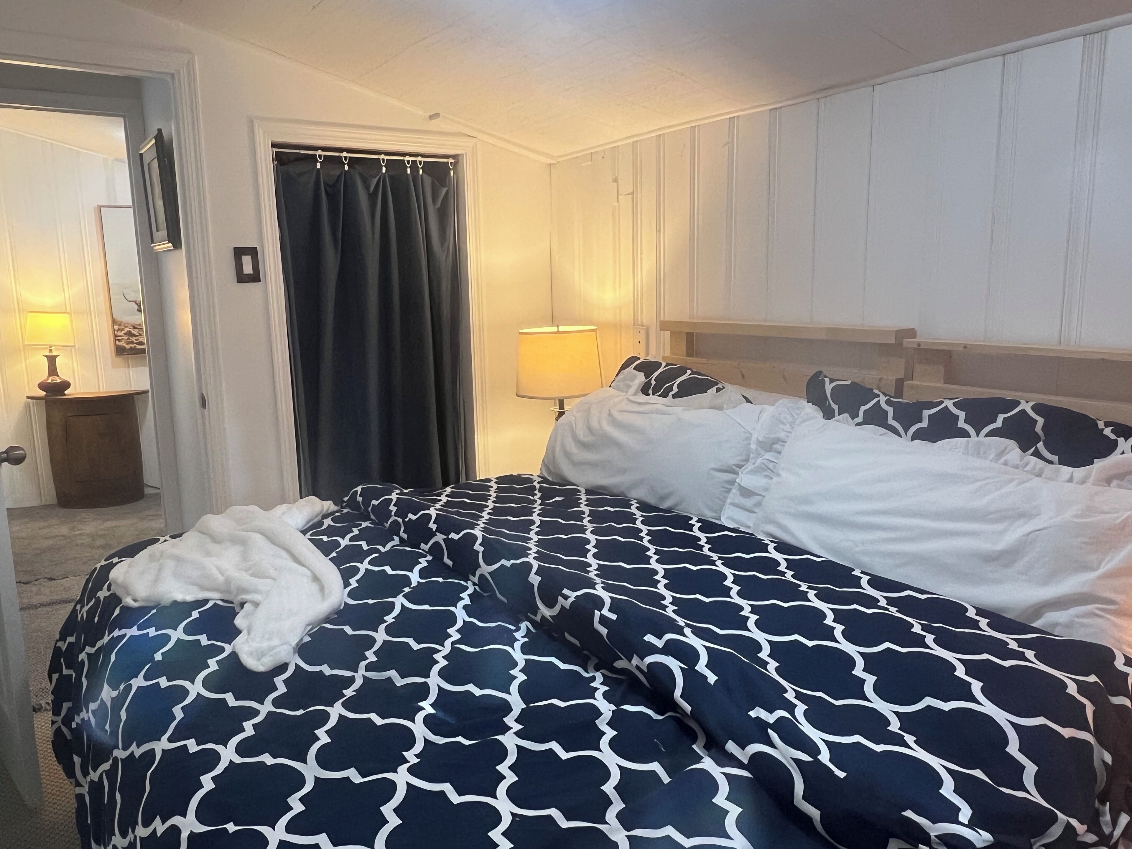 A hotel room with a bed, a nightstand, a lamp, a door, and a curtain.