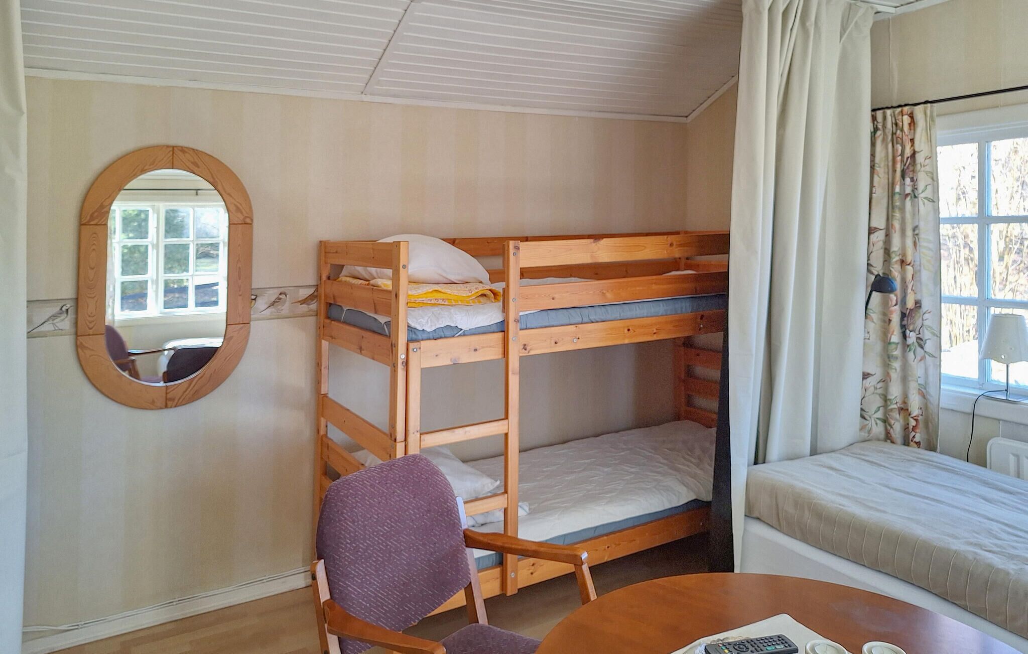 A bunk bed room with a wooden chair, a round mirror, and a window with curtains.