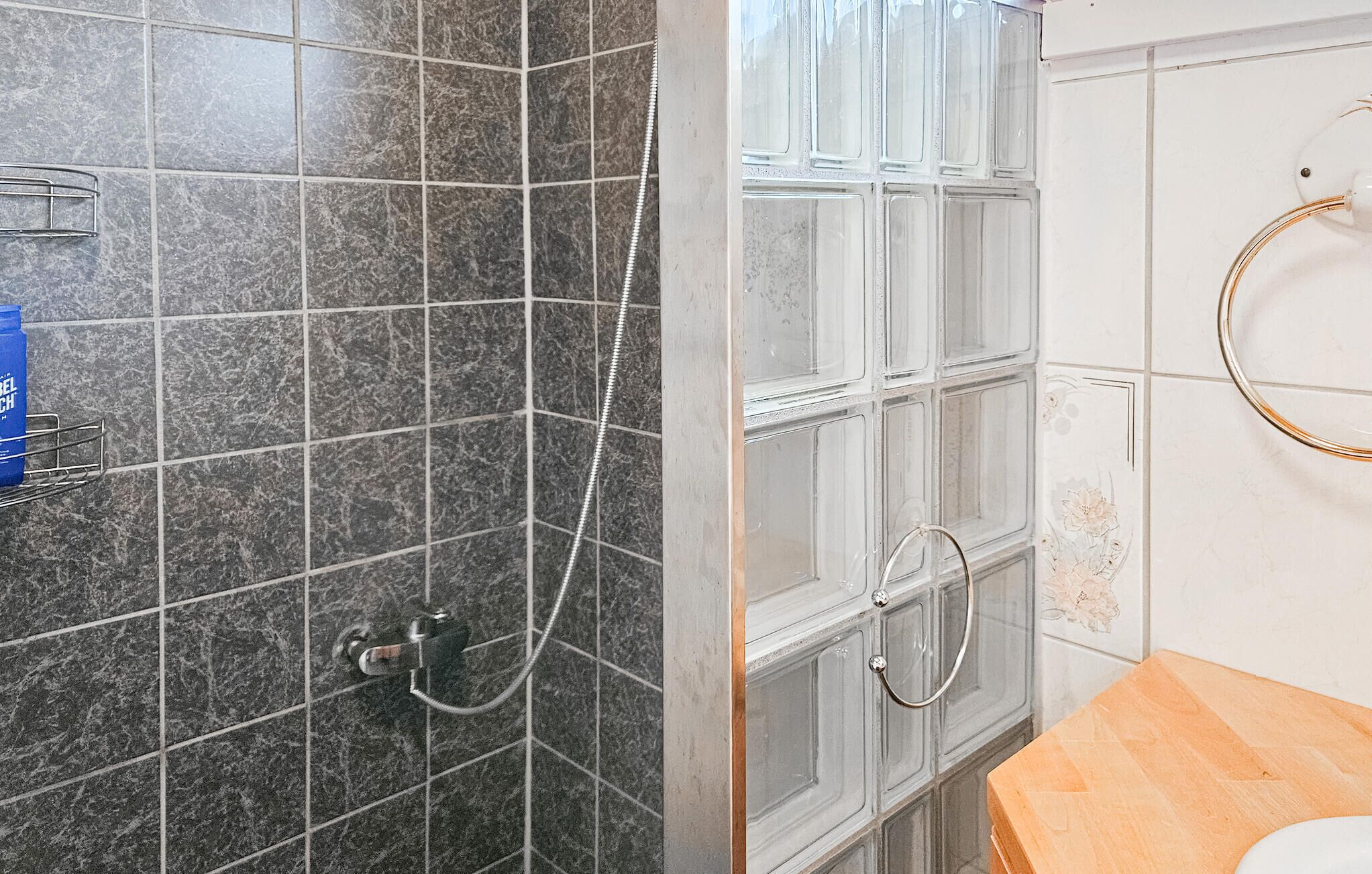A bathroom with dark marble tiles, a shower with a glass door, and a toilet with a wooden vanity.