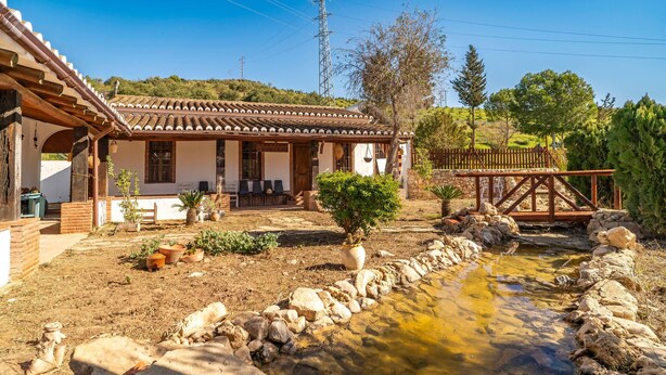 A traditional house with a tiled roof, a patio with chairs, a small pond, and a wooden bridge. - Beautiful home in Alora with WiFi (Alora)