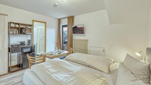 Une chambre d’hôtel compacte comprenant un coin cuisine, un lit avec du linge de maison blanc, une table à manger et une vue sur l’extérieur par une fenêtre.