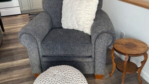 A grey armchair with a white pillow, a round white pouf, and a small wooden table in a modern kitchen with white cabinets and a wooden staircase. - Cozy, Clean & Convenient 1-bedroom apartment with AC & WiFi in charming Clayton (Clayton)