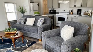Un salon moderne avec des canapés gris, une table basse en bois et un pouf rond.