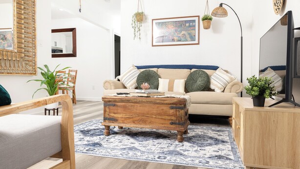 Een woonkamer met een bank, een houten salontafel, een bijzettafeltje en een hangplant.
