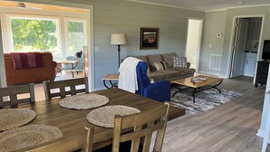 Un vaste salon avec une table à manger en bois, des canapés bleus et bruns, et un coin cuisine à l’arrière-plan.