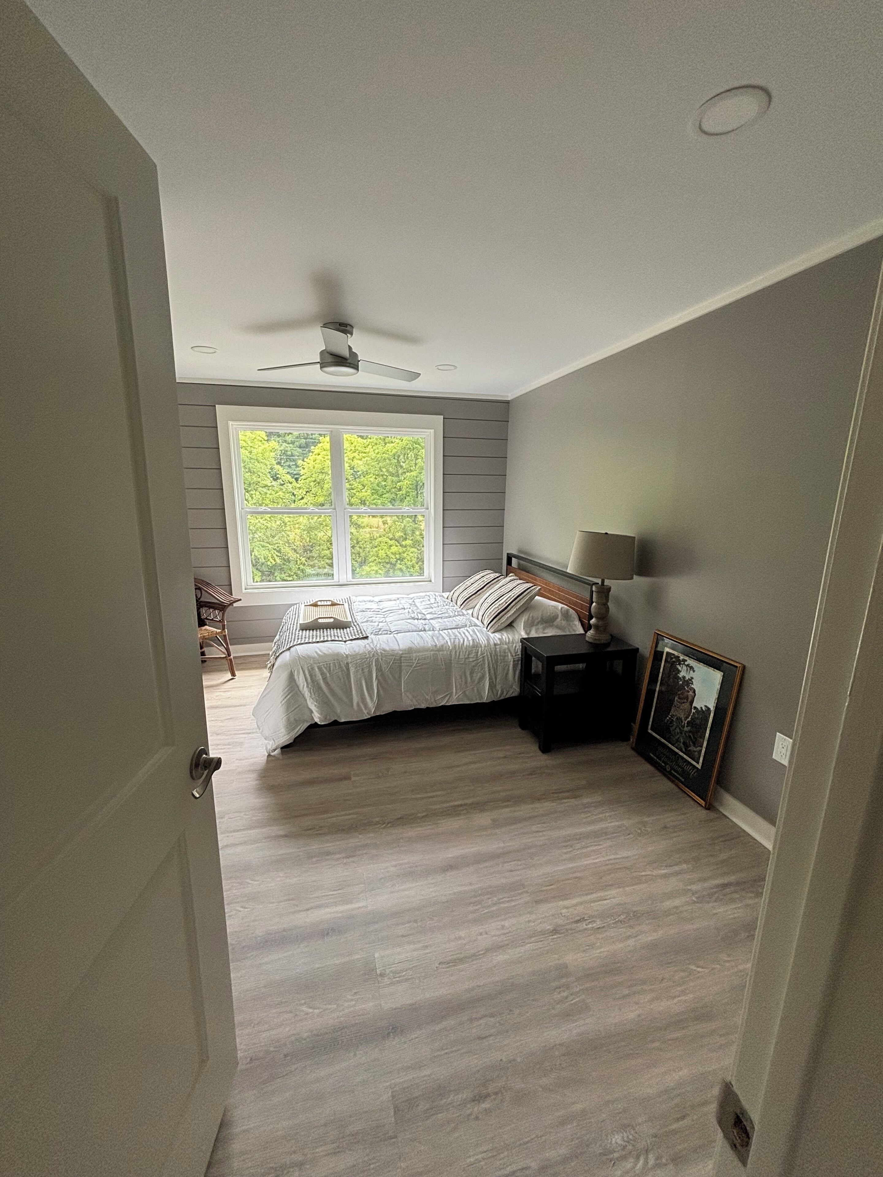 Un dormitorio con cama, mesita de noche, ventilador de techo, ventana y puerta.