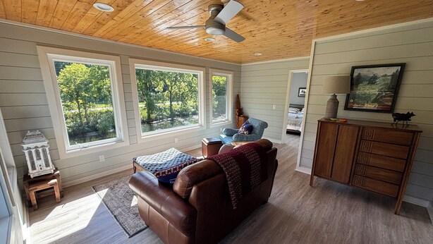 Un salon spacieux avec un canapé en cuir marron, un plafond en bois et de grandes fenêtres donnant sur un paysage verdoyant.