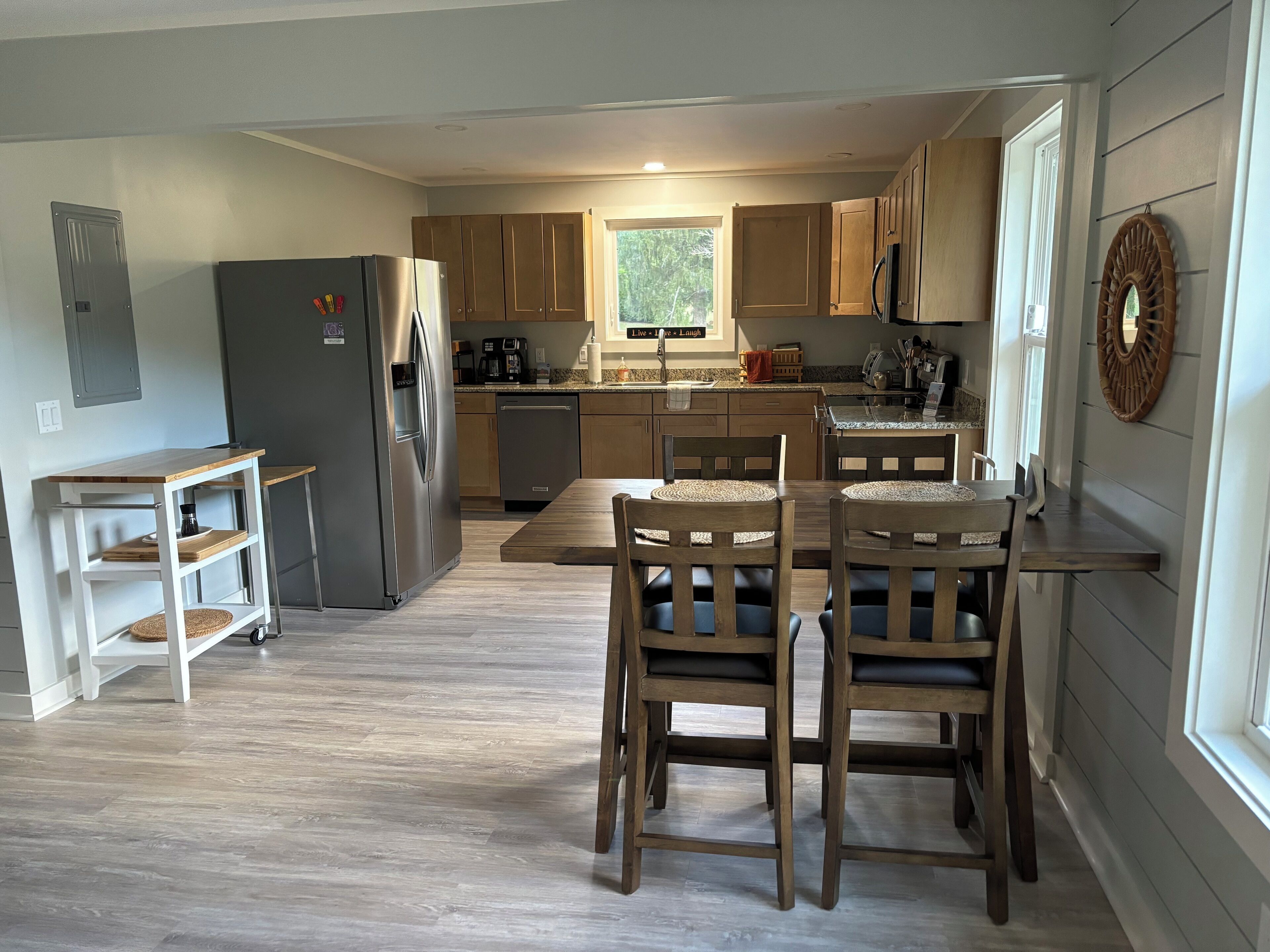 Une cuisine moderne avec des meubles en bois, un réfrigérateur en acier inoxydable et un coin repas comprenant une table et des chaises en bois.