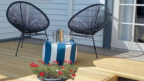 A patio area with two black chairs, a striped table, and a potted plant with red flowers. - Magpie Cottage. Newly Renovated , 2 Bed, 2 bathroom close to Napier CBD (Napier)