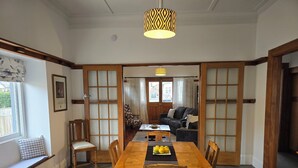 A traditional Japanese-style room with tatami mat flooring, a low wooden table with chairs, a sliding glass door leading to a living area with a sofa and cushions, and a hanging lamp. - Magpie Cottage. Newly Renovated , 2 Bed, 2 bathroom close to Napier CBD (Napier)