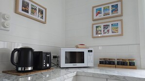A modern kitchen with a white microwave, a black coffee maker, and a coffee station with labeled jars. - Magpie Cottage. Newly Renovated , 2 Bed, 2 bathroom close to Napier CBD (Napier)