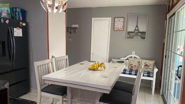 Une cuisine équipée d’une table à manger, de chaises, d’un réfrigérateur et d’un luminaire suspendu.