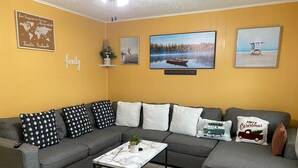 Un salon avec un canapé d’angle gris, une table basse en marbre et une carte du monde accrochée au mur.