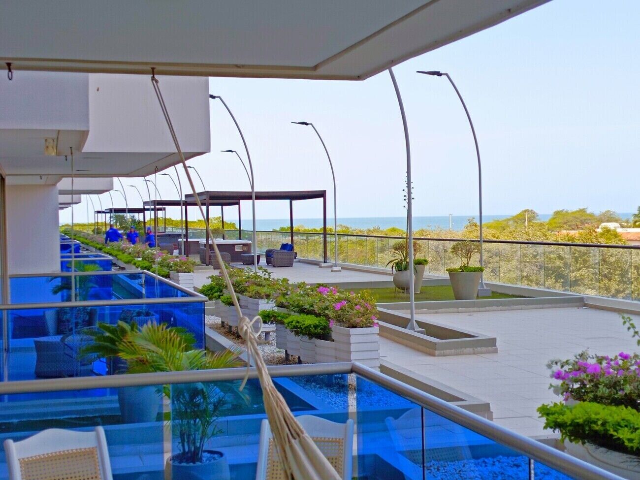 A rooftop pool area with a clear view of the sea, outdoor seating, and potted plants.