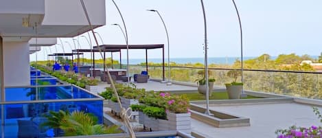 A rooftop pool area with a clear view of the sea, outdoor seating, and potted plants.