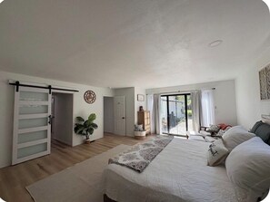 A bedroom with a bed, a sliding door, a plant, a window, and a view of the outside. - Hot Tub • Tree Fort • Game Room • 2 Master Suites • Near Bandon Dunes (Coos Bay)