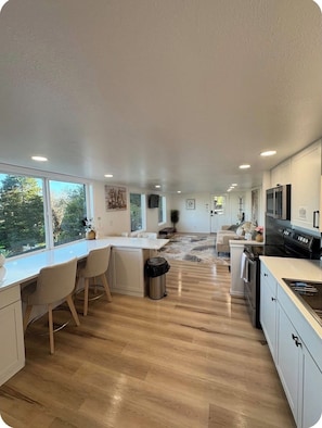 A modern kitchen with a central island, wooden flooring, and large windows. - Hot Tub • Tree Fort • Game Room • 2 Master Suites • Near Bandon Dunes (Coos Bay)
