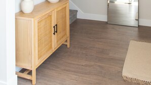 Un pasillo con un aparador de madera, una planta en maceta y un espejo que refleja una habitación con cama.