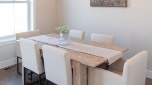 Un comedor con una mesa de madera, sillas blancas y una araña.