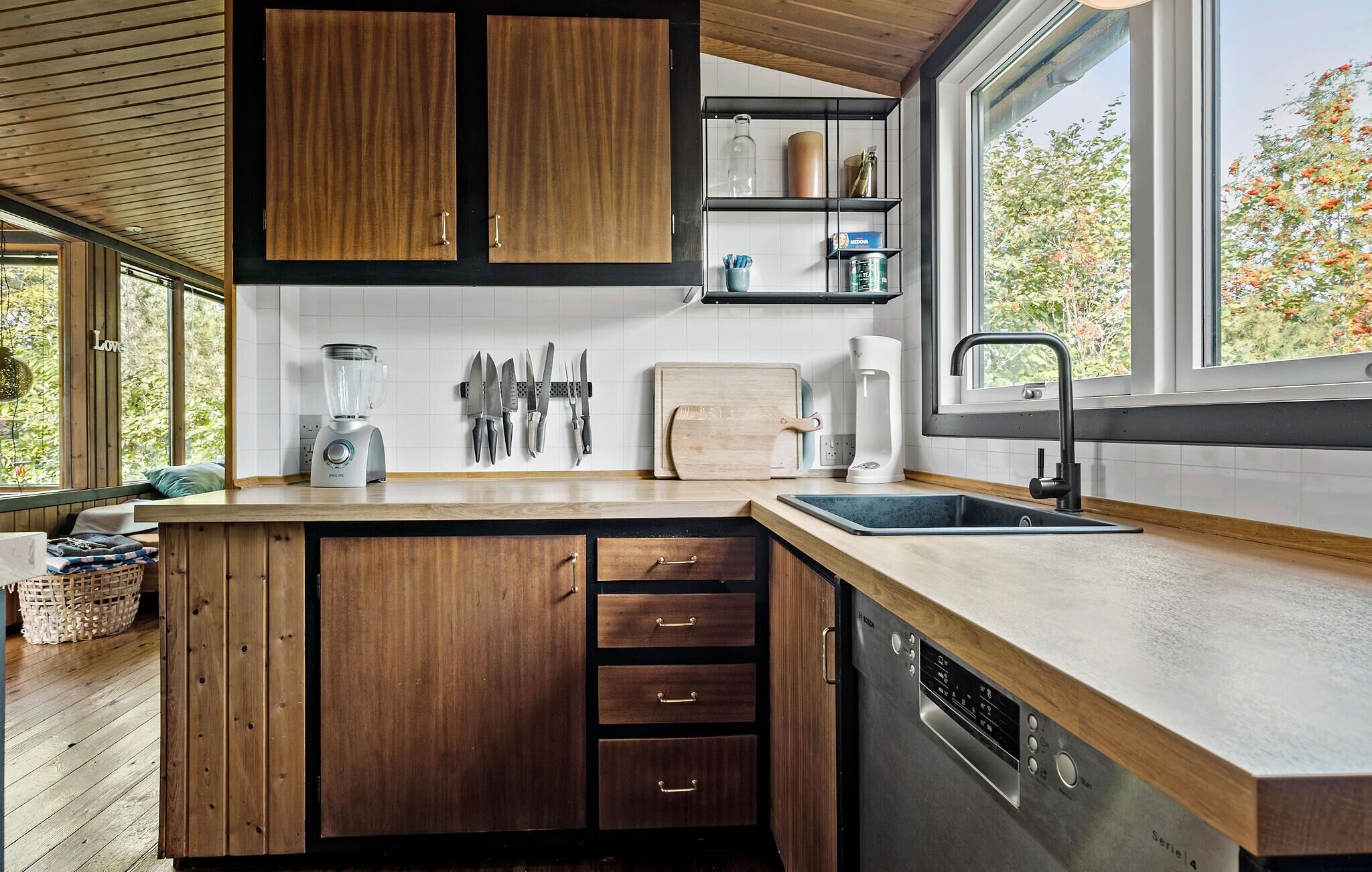 Een moderne keuken met houten kastjes, een inbouwvaatwasser, een spoelbak en een raam met uitzicht op groen.
