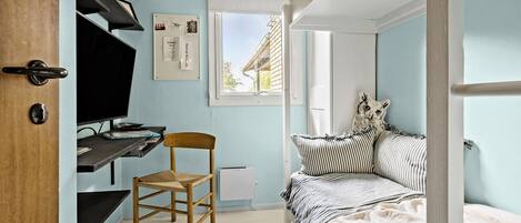 A bedroom with a bed, a desk, a chair, and a window.