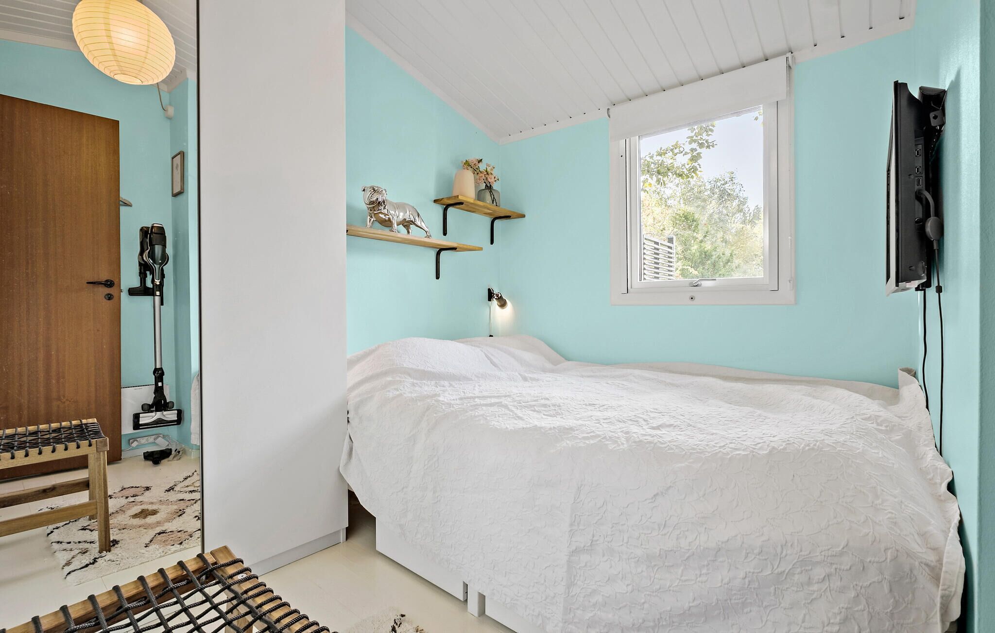 Une chambre à coucher avec un lit, une fenêtre, une étagère ornée d’objets décoratifs et une porte.