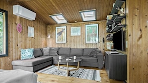 A cozy living room with a gray sectional sofa, a small round coffee table, and a TV stand. There are framed pictures on the wall, a ceiling fan, and a skylight. - Nice home in Gørlev with WiFi (Gørlev)