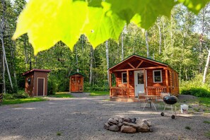Une cabane avec une véranda et un foyer, située dans un cadre forestier.