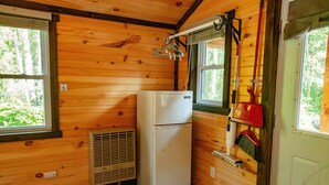 A compact kitchen with wooden walls, a white refrigerator, a window with a view of greenery, and a broom hanging on the wall.