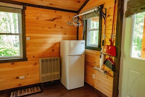 Cocina compacta con paredes de madera, un refrigerador blanco, una ventana con vistas a zonas verdes y una escoba colgada en la pared.
