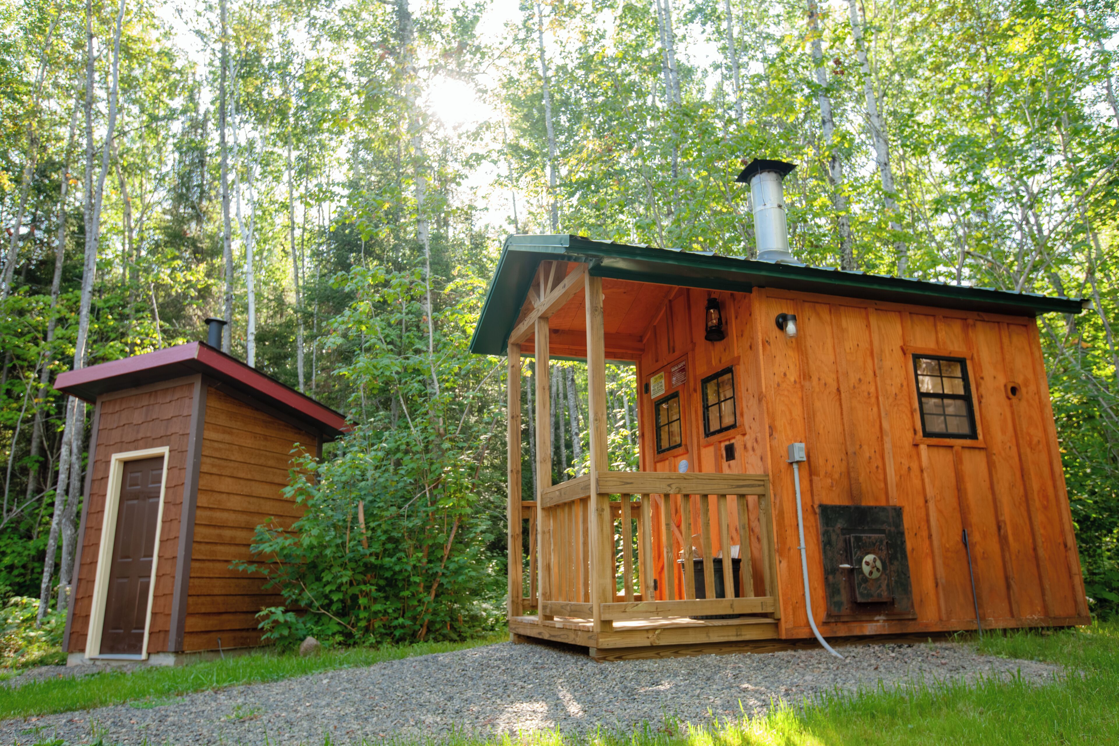 Une cabane en bois dotée d’un porche et d’une cheminée, entourée d’arbres.